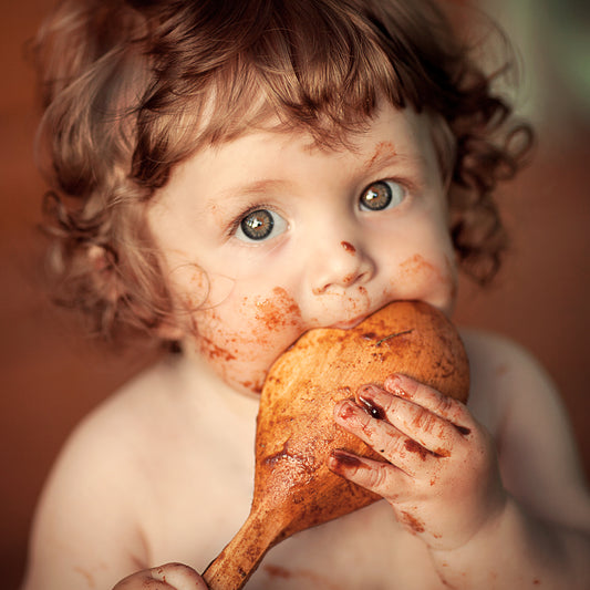 A cute toddler covered in jelly from eating it off of a handmade wood spoon
