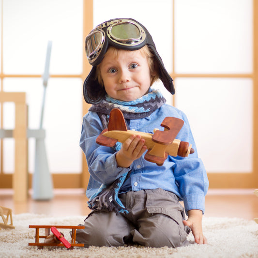 Funny kid wearing flight goggles playing with a handmade wooden toy ariplane
