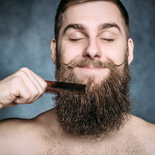 Handsome happy smiling man with funny mustache and closed eyes combing his big beard. Beard care | LocalWe