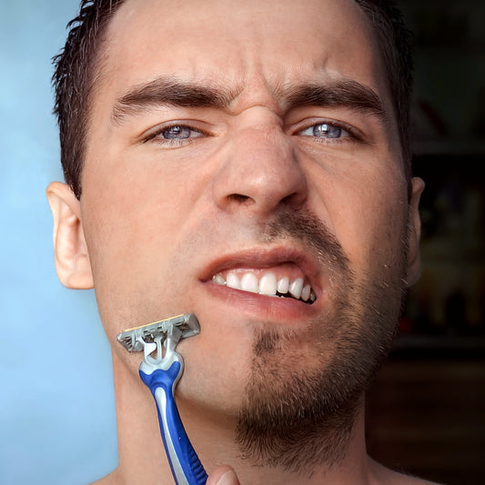 Young man with half of his face shaved holds his razor and frets over whether or not he wants to celebrate Movember or No-Shave November