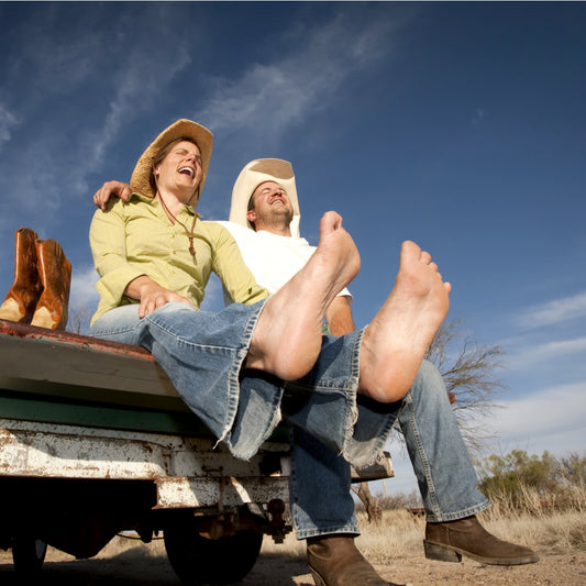 A woman laughs sitting on the back of a pickup truck in her bare feet after taking off her cowboy boots